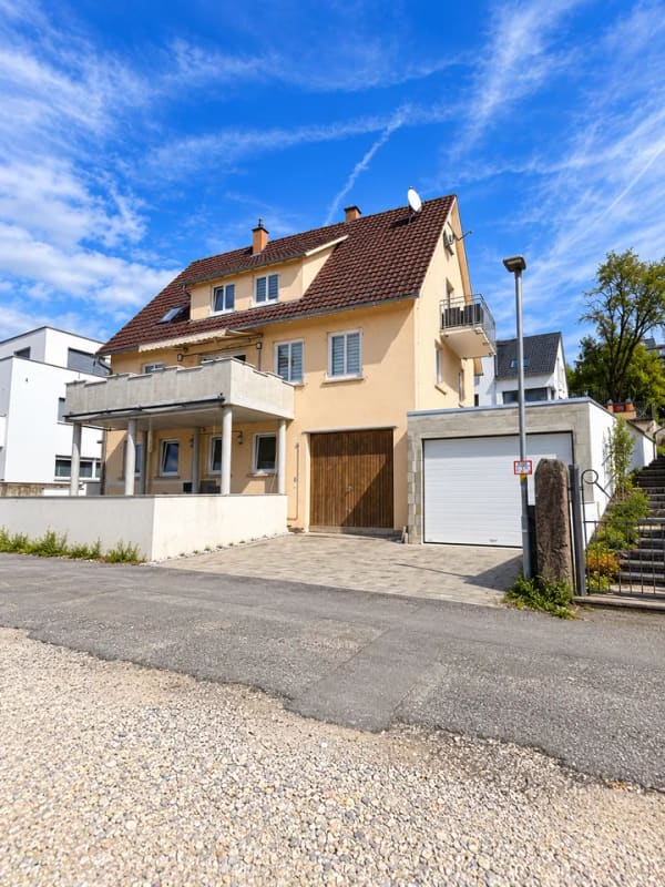 Immobilie in Neckartenzlingen - Dieses großzügige und vielseitig nutzbare Haus in Neckartenzlingen bietet viel Platz für Familien, Mehrgenerationenwohnen oder die Kombination aus Eigennutzung und Vermietung.  Die Immobilie verfügt über eine großzügige Raumaufteilung mit zahlreichen Zimmern und bietet dadurch vielfältige Möglichkeiten zur individuellen Gestaltung und Nutzung.  Ein besonderes Highlight ist die separate 2-Zimmer-Wohnung im unteren Bereich des Hauses. Diese eignet sich ideal zur Vermietung und verfügt über eine großzügige Terrasse mit ca. 25 m². Somit besteht die attraktive Möglichkeit, einen Teil des Hauses separat zu vermieten und zusätzliche Mieteinnahmen zu erzielen.  Die obere Wohneinheit bietet ebenfalls viel Platz und verfügt über einen großzügigen Balkon mit ca. 18 m², der zusätzlichen Freiraum im Außenbereich schafft.  Zum Haus gehören außerdem zwei große Garagen, die komfortable Stellmöglichkeiten für Fahrzeuge sowie zusätzlichen Stauraum bieten.  Die Lage ist besonders für Familien interessant: Eine Schule befindet sich direkt gegenüber, sodass der Schulweg besonders kurz ist. Auch ein Kindergarten befindet sich in der Nähe. Einrichtungen des täglichen Bedarfs sowie weitere Angebote sind gut erreichbar.  Insgesamt bietet diese Immobilie eine interessante Kombination aus großzügigem Wohnraum, separater Wohneinheit, attraktiven Außenflächen und vielseitigen Nutzungsmöglichkeiten. Besonders für größere Familien, Mehrgenerationenwohnen oder Käufer, die Wohnen und Vermietung miteinander verbinden möchten, bietet das Haus hervorragende Voraussetzungen. - Bild 0