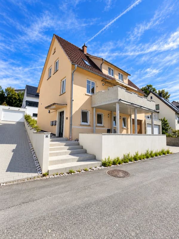 Immobilie in Neckartenzlingen - Dieses großzügige und vielseitig nutzbare Haus in Neckartenzlingen bietet viel Platz für Familien, Mehrgenerationenwohnen oder die Kombination aus Eigennutzung und Vermietung.  Die Immobilie verfügt über eine großzügige Raumaufteilung mit zahlreichen Zimmern und bietet dadurch vielfältige Möglichkeiten zur individuellen Gestaltung und Nutzung.  Ein besonderes Highlight ist die separate 2-Zimmer-Wohnung im unteren Bereich des Hauses. Diese eignet sich ideal zur Vermietung und verfügt über eine großzügige Terrasse mit ca. 25 m². Somit besteht die attraktive Möglichkeit, einen Teil des Hauses separat zu vermieten und zusätzliche Mieteinnahmen zu erzielen.  Die obere Wohneinheit bietet ebenfalls viel Platz und verfügt über einen großzügigen Balkon mit ca. 18 m², der zusätzlichen Freiraum im Außenbereich schafft.  Zum Haus gehören außerdem zwei große Garagen, die komfortable Stellmöglichkeiten für Fahrzeuge sowie zusätzlichen Stauraum bieten.  Die Lage ist besonders für Familien interessant: Eine Schule befindet sich direkt gegenüber, sodass der Schulweg besonders kurz ist. Auch ein Kindergarten befindet sich in der Nähe. Einrichtungen des täglichen Bedarfs sowie weitere Angebote sind gut erreichbar.  Insgesamt bietet diese Immobilie eine interessante Kombination aus großzügigem Wohnraum, separater Wohneinheit, attraktiven Außenflächen und vielseitigen Nutzungsmöglichkeiten. Besonders für größere Familien, Mehrgenerationenwohnen oder Käufer, die Wohnen und Vermietung miteinander verbinden möchten, bietet das Haus hervorragende Voraussetzungen. - Bild 1