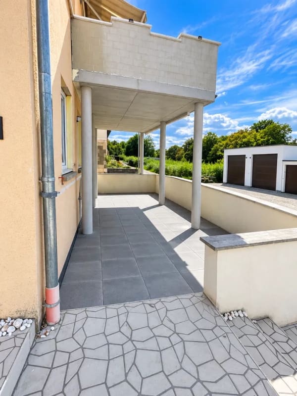 Immobilie in Neckartenzlingen - Dieses großzügige und vielseitig nutzbare Haus in Neckartenzlingen bietet viel Platz für Familien, Mehrgenerationenwohnen oder die Kombination aus Eigennutzung und Vermietung.  Die Immobilie verfügt über eine großzügige Raumaufteilung mit zahlreichen Zimmern und bietet dadurch vielfältige Möglichkeiten zur individuellen Gestaltung und Nutzung.  Ein besonderes Highlight ist die separate 2-Zimmer-Wohnung im unteren Bereich des Hauses. Diese eignet sich ideal zur Vermietung und verfügt über eine großzügige Terrasse mit ca. 25 m². Somit besteht die attraktive Möglichkeit, einen Teil des Hauses separat zu vermieten und zusätzliche Mieteinnahmen zu erzielen.  Die obere Wohneinheit bietet ebenfalls viel Platz und verfügt über einen großzügigen Balkon mit ca. 18 m², der zusätzlichen Freiraum im Außenbereich schafft.  Zum Haus gehören außerdem zwei große Garagen, die komfortable Stellmöglichkeiten für Fahrzeuge sowie zusätzlichen Stauraum bieten.  Die Lage ist besonders für Familien interessant: Eine Schule befindet sich direkt gegenüber, sodass der Schulweg besonders kurz ist. Auch ein Kindergarten befindet sich in der Nähe. Einrichtungen des täglichen Bedarfs sowie weitere Angebote sind gut erreichbar.  Insgesamt bietet diese Immobilie eine interessante Kombination aus großzügigem Wohnraum, separater Wohneinheit, attraktiven Außenflächen und vielseitigen Nutzungsmöglichkeiten. Besonders für größere Familien, Mehrgenerationenwohnen oder Käufer, die Wohnen und Vermietung miteinander verbinden möchten, bietet das Haus hervorragende Voraussetzungen. - Bild 2