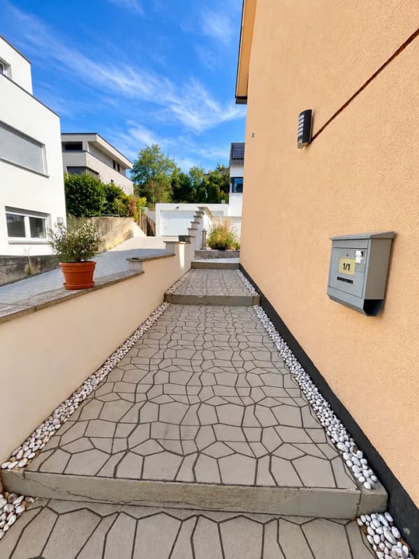 Immobilie in Neckartenzlingen - Dieses großzügige und vielseitig nutzbare Haus in Neckartenzlingen bietet viel Platz für Familien, Mehrgenerationenwohnen oder die Kombination aus Eigennutzung und Vermietung.  Die Immobilie verfügt über eine großzügige Raumaufteilung mit zahlreichen Zimmern und bietet dadurch vielfältige Möglichkeiten zur individuellen Gestaltung und Nutzung.  Ein besonderes Highlight ist die separate 2-Zimmer-Wohnung im unteren Bereich des Hauses. Diese eignet sich ideal zur Vermietung und verfügt über eine großzügige Terrasse mit ca. 25 m². Somit besteht die attraktive Möglichkeit, einen Teil des Hauses separat zu vermieten und zusätzliche Mieteinnahmen zu erzielen.  Die obere Wohneinheit bietet ebenfalls viel Platz und verfügt über einen großzügigen Balkon mit ca. 18 m², der zusätzlichen Freiraum im Außenbereich schafft.  Zum Haus gehören außerdem zwei große Garagen, die komfortable Stellmöglichkeiten für Fahrzeuge sowie zusätzlichen Stauraum bieten.  Die Lage ist besonders für Familien interessant: Eine Schule befindet sich direkt gegenüber, sodass der Schulweg besonders kurz ist. Auch ein Kindergarten befindet sich in der Nähe. Einrichtungen des täglichen Bedarfs sowie weitere Angebote sind gut erreichbar.  Insgesamt bietet diese Immobilie eine interessante Kombination aus großzügigem Wohnraum, separater Wohneinheit, attraktiven Außenflächen und vielseitigen Nutzungsmöglichkeiten. Besonders für größere Familien, Mehrgenerationenwohnen oder Käufer, die Wohnen und Vermietung miteinander verbinden möchten, bietet das Haus hervorragende Voraussetzungen. - Bild 3
