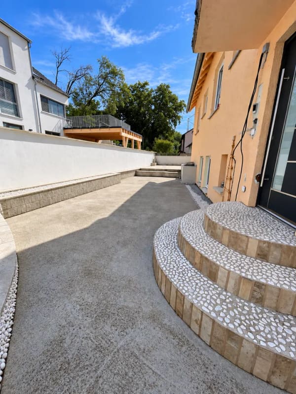 Immobilie in Neckartenzlingen - Dieses großzügige und vielseitig nutzbare Haus in Neckartenzlingen bietet viel Platz für Familien, Mehrgenerationenwohnen oder die Kombination aus Eigennutzung und Vermietung.  Die Immobilie verfügt über eine großzügige Raumaufteilung mit zahlreichen Zimmern und bietet dadurch vielfältige Möglichkeiten zur individuellen Gestaltung und Nutzung.  Ein besonderes Highlight ist die separate 2-Zimmer-Wohnung im unteren Bereich des Hauses. Diese eignet sich ideal zur Vermietung und verfügt über eine großzügige Terrasse mit ca. 25 m². Somit besteht die attraktive Möglichkeit, einen Teil des Hauses separat zu vermieten und zusätzliche Mieteinnahmen zu erzielen.  Die obere Wohneinheit bietet ebenfalls viel Platz und verfügt über einen großzügigen Balkon mit ca. 18 m², der zusätzlichen Freiraum im Außenbereich schafft.  Zum Haus gehören außerdem zwei große Garagen, die komfortable Stellmöglichkeiten für Fahrzeuge sowie zusätzlichen Stauraum bieten.  Die Lage ist besonders für Familien interessant: Eine Schule befindet sich direkt gegenüber, sodass der Schulweg besonders kurz ist. Auch ein Kindergarten befindet sich in der Nähe. Einrichtungen des täglichen Bedarfs sowie weitere Angebote sind gut erreichbar.  Insgesamt bietet diese Immobilie eine interessante Kombination aus großzügigem Wohnraum, separater Wohneinheit, attraktiven Außenflächen und vielseitigen Nutzungsmöglichkeiten. Besonders für größere Familien, Mehrgenerationenwohnen oder Käufer, die Wohnen und Vermietung miteinander verbinden möchten, bietet das Haus hervorragende Voraussetzungen. - Bild 4